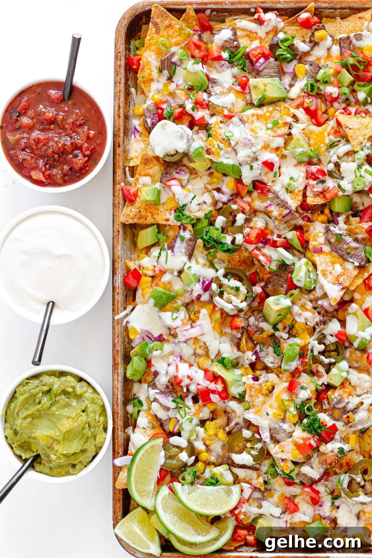 Loaded Steak Nachos Recipe with Melted Cheese 8 Steak nachos on a sheet pan with small bowls of salsa, sour cream and guacamole beside it.