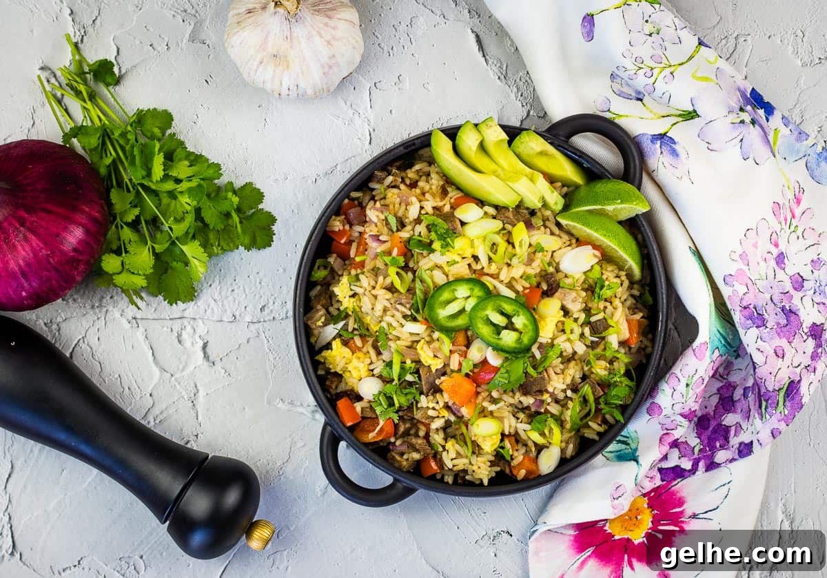 A cast-iron pan filled with Brisket Fried Rice, garnished with sliced avocado, lime wedges, jalapeño slices, and fresh cilantro.