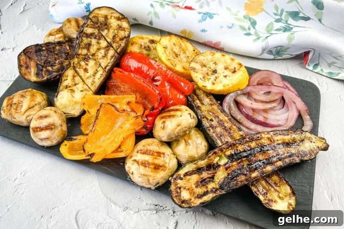 Grilled vegetables including zucchini, mushrooms, red onions, peppers, and squash, arranged on a rectangular black platter.