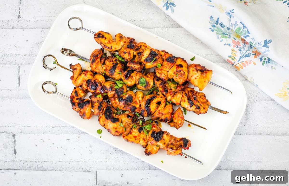 A rectangular white plate with four Sweet & Spicy Grilled Harissa-Honey Chicken Skewers garnished with chopped herbs.
