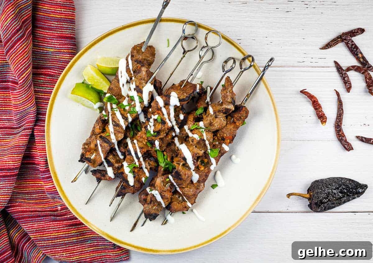 Grilled Steak skewers on a white plate with chilis nearby.
