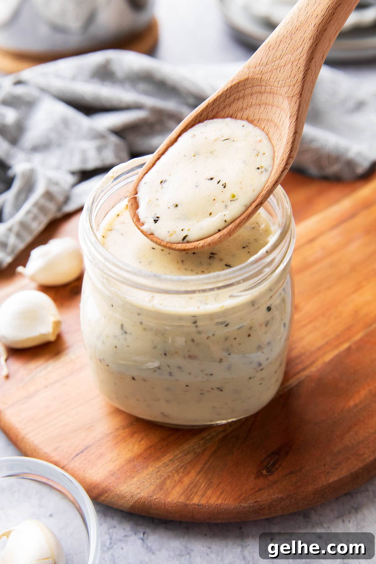 Homemade Creamy Garlic Parmesan Sauce 2 A wooden spoon filled with garlic parmesan sauce to showcase its thick and creamy texture that’s perfect for pouring over pasta, as a pizza sauce, and as wing sauce.